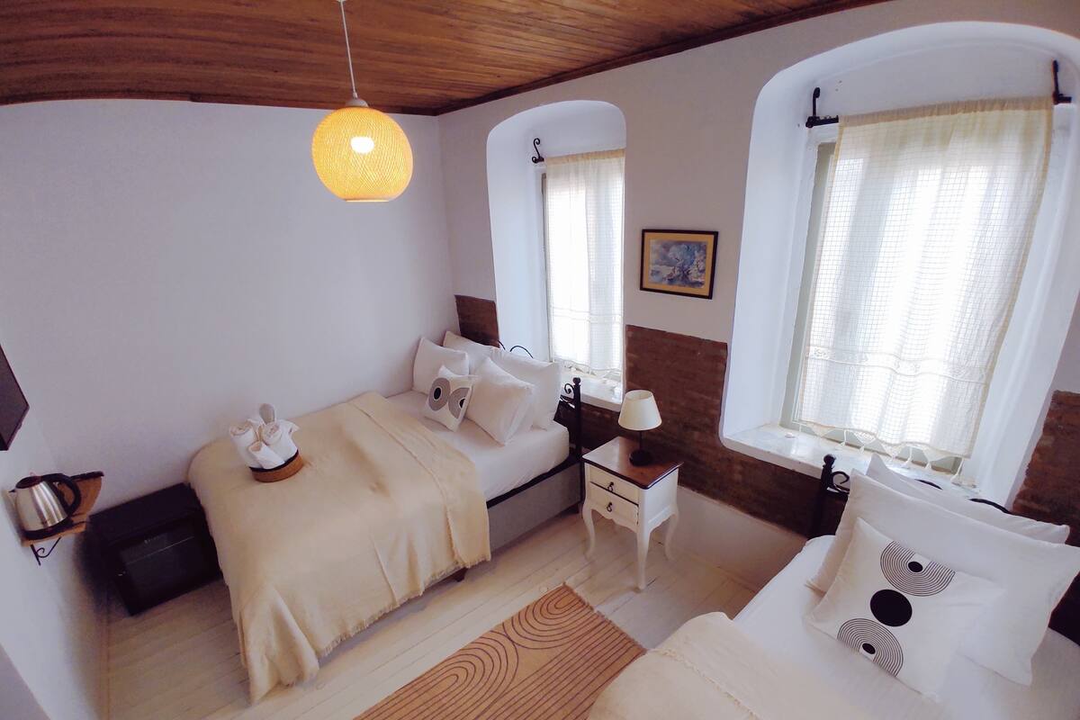 A room with a bed, a bedside table, a lamp, and a window with curtains.