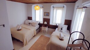 Una habitación con dos camas, techo de madera, lámpara colgante y ventana con cortinas.