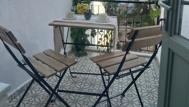 Un balcón con una mesa y sillas, vista a un árbol y un piso con diseño.