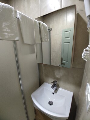 A compact bathroom with a sink and mirror, featuring a towel rack and tile walls.