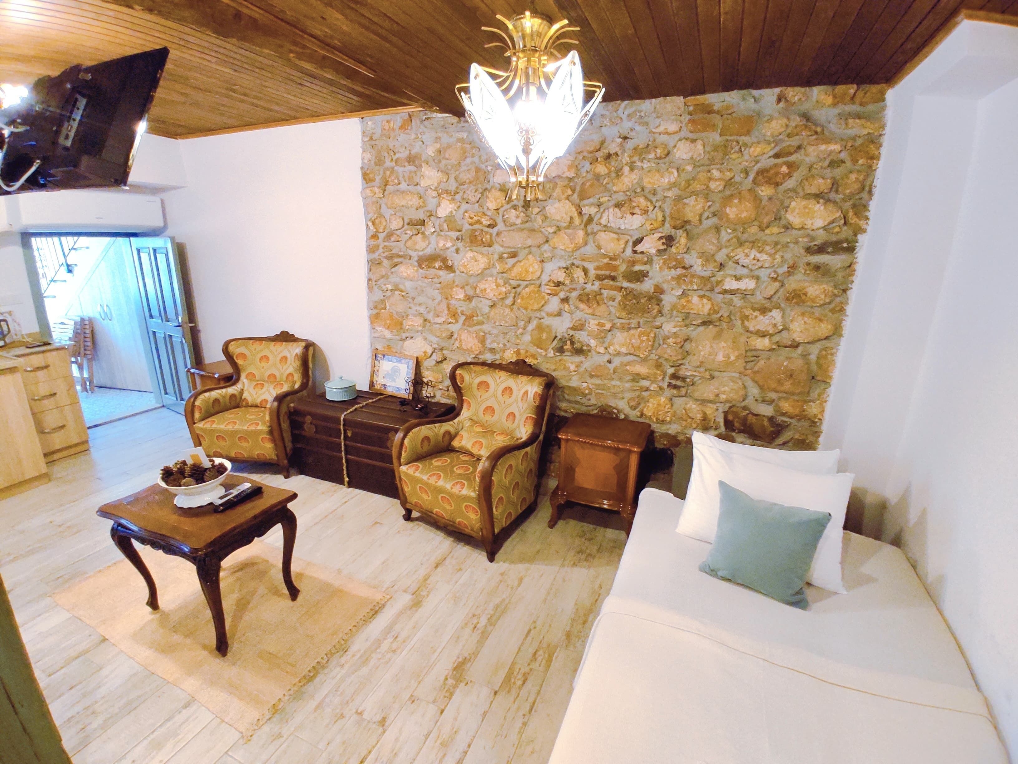 Un salon avec un mur en pierre, deux fauteuils, un canapé, une table basse en bois et un lustre.