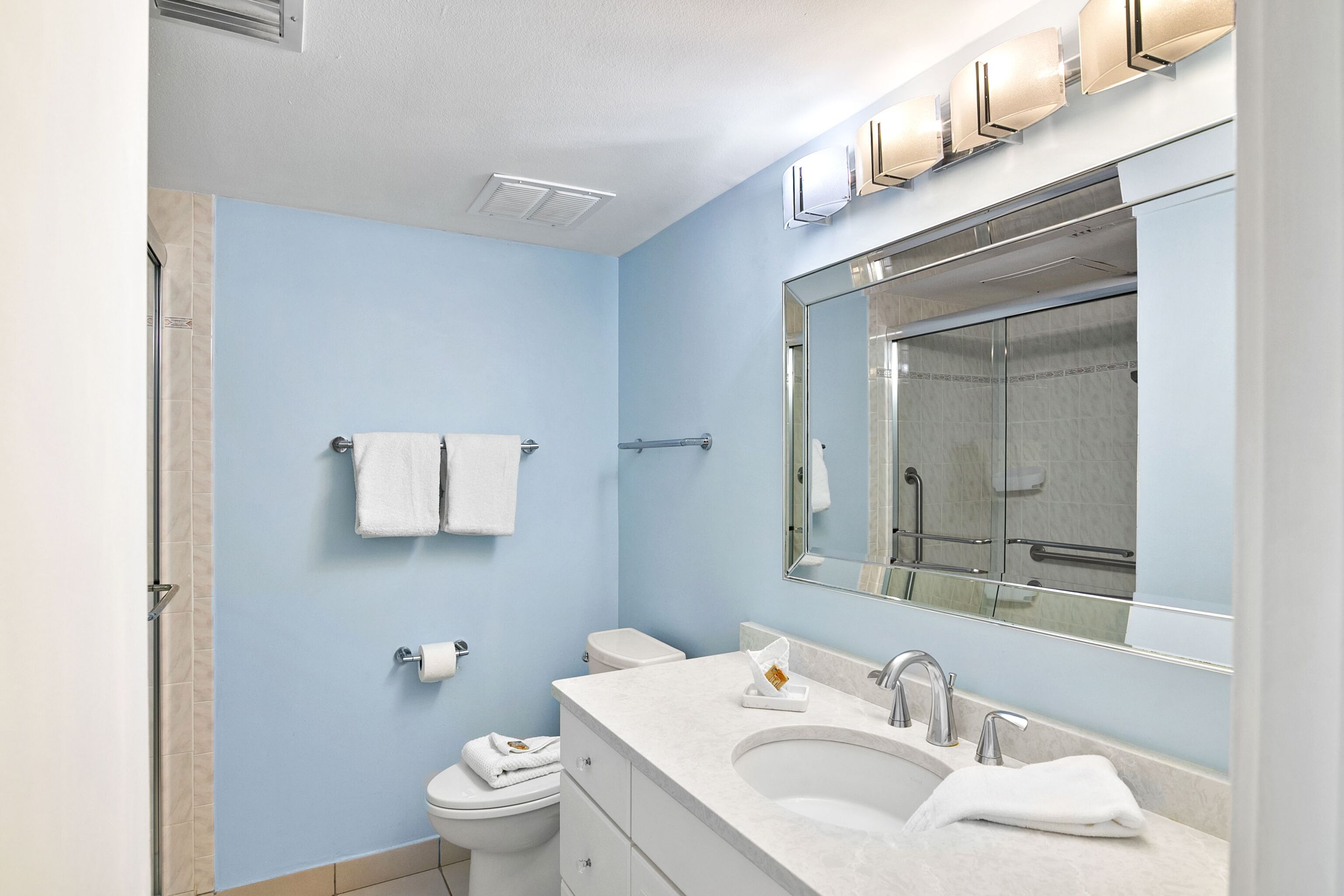 Une salle de bain avec un lavabo blanc, un grand miroir et des toilettes.