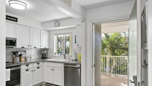 Una cocina moderna con armarios blancos, electrodomésticos de acero inoxidable y vistas a un balcón con barandilla blanca.