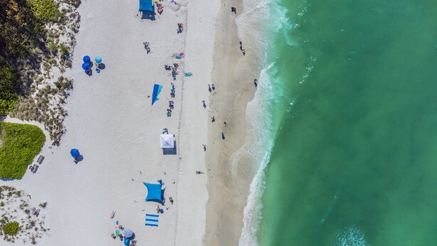 Vista aérea de una playa con tiendas de campaña, sombrillas y gente.