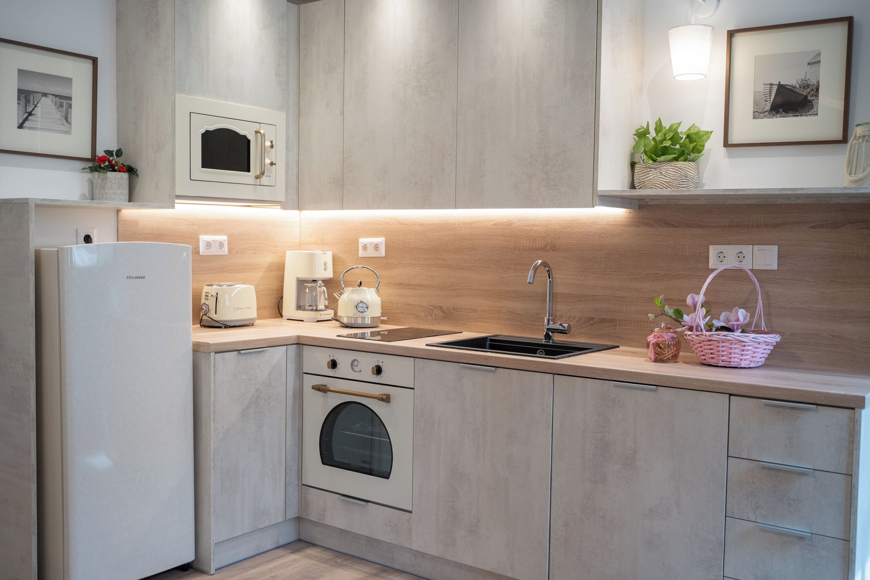 A modern kitchen with a built-in microwave, oven, and sink. There are framed pictures on the wall and a basket with flowers on the countertop.