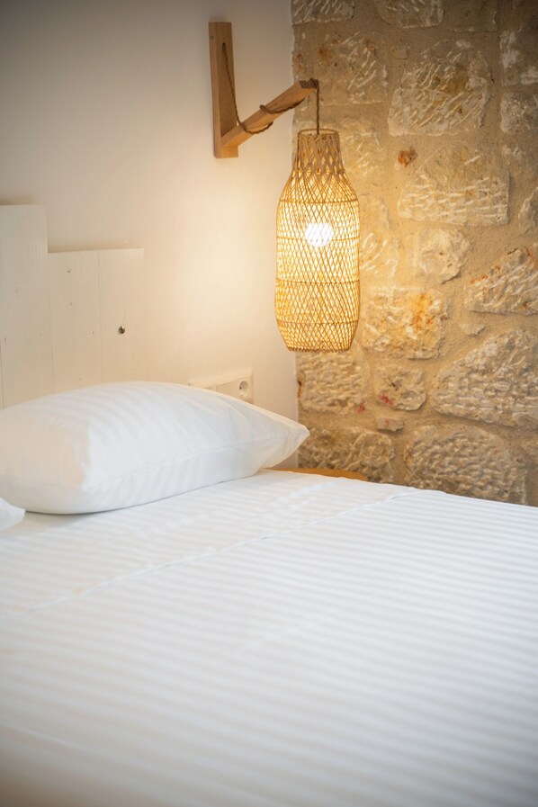 A bed with white bedding, a white pillow, and a wall-mounted light fixture. - Olvio Suites (West Mani)