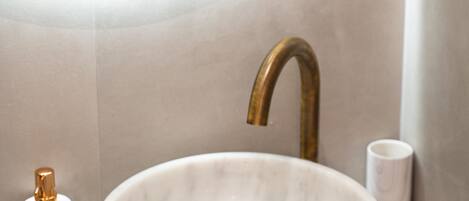 A bathroom with a round marble sink, a gold faucet, and a white marble cup on the counter.
