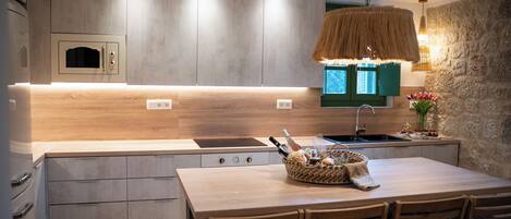 A modern kitchen with wooden cabinets, a built-in oven, a stone accent wall, and a dining area with a table and chairs.