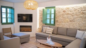 A modern living room with a stone wall, a fireplace, and a large sofa. - Olvio Suites (West Mani)