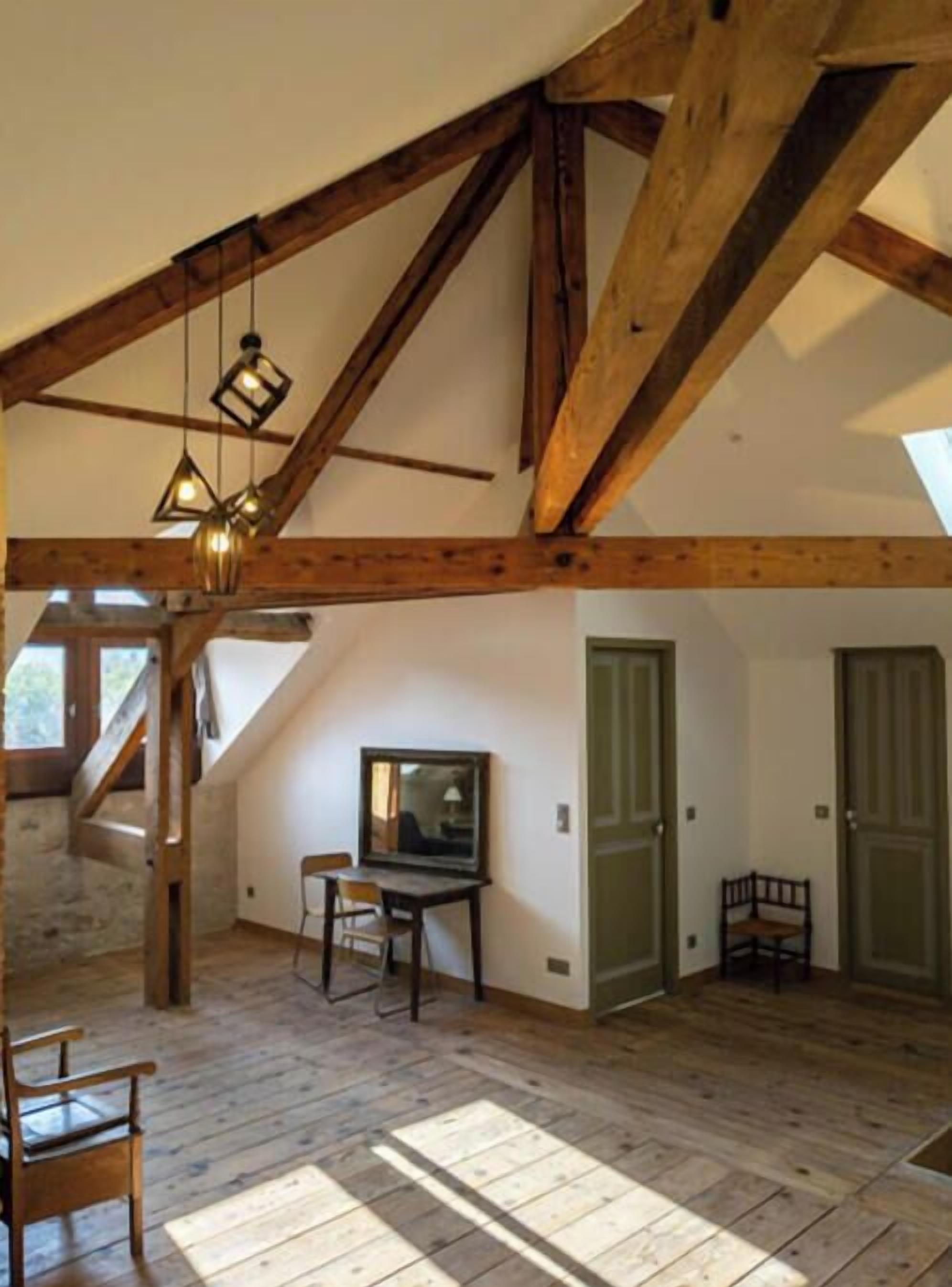 A spacious attic room with exposed wooden beams, a loft bed, a desk, and a chair.
