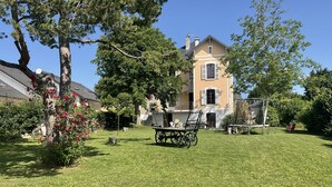 Una casa grande con un césped cuidado, un carromato de madera y una pérgola.