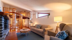 A cozy living room with a stone fireplace, a wooden spiral staircase, a sofa, a coffee table, and a lamp. - Appartamento La Chiocciola by Wonderful Italy (Bellagio)