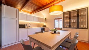A modern kitchen with white cabinets, a central island with chairs, a hanging light fixture, and a wine display cabinet. - Appartamento La Chiocciola by Wonderful Italy (Bellagio)