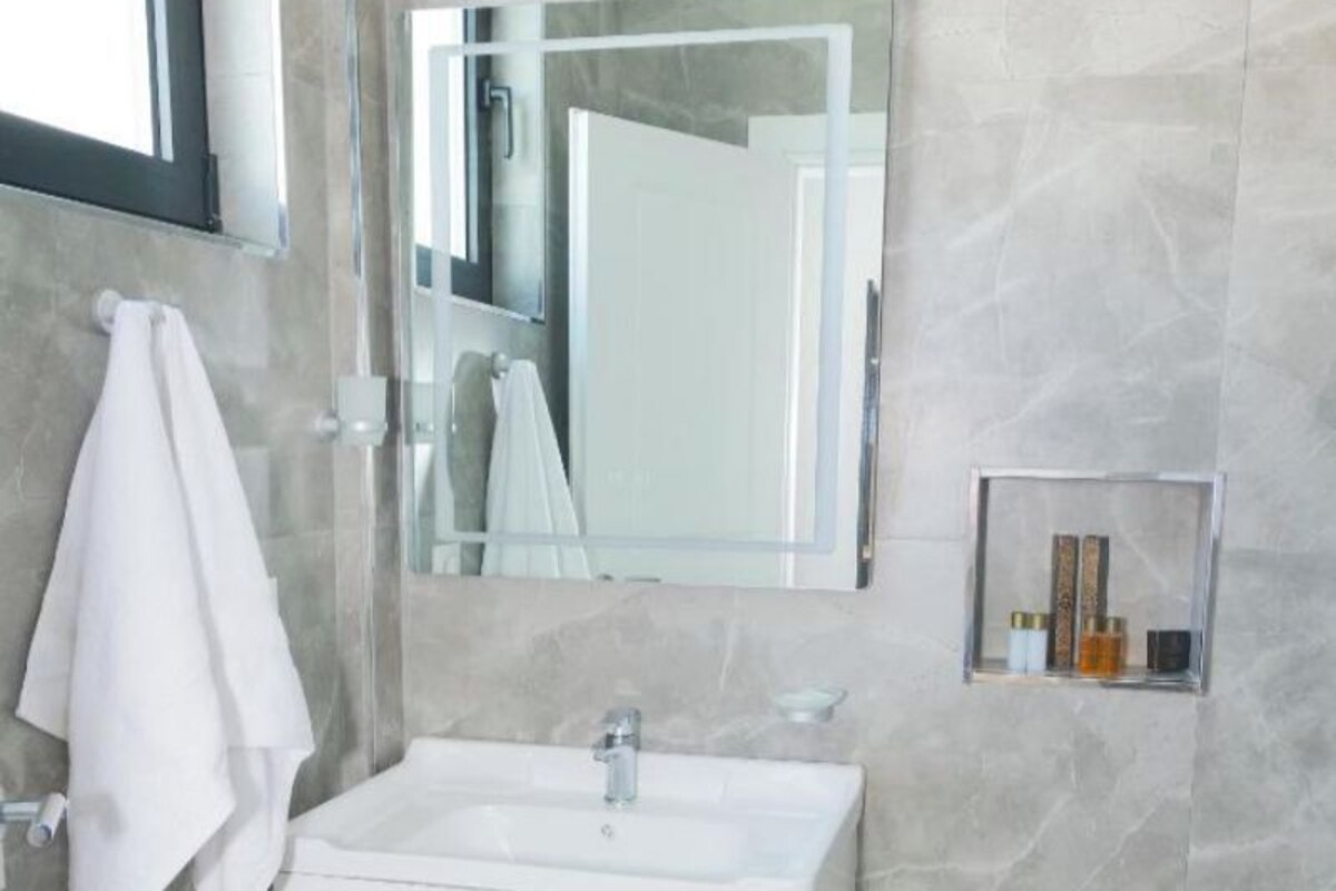 Un baño con un lavamanos blanco, un espejo y una toalla colgada en la pared.