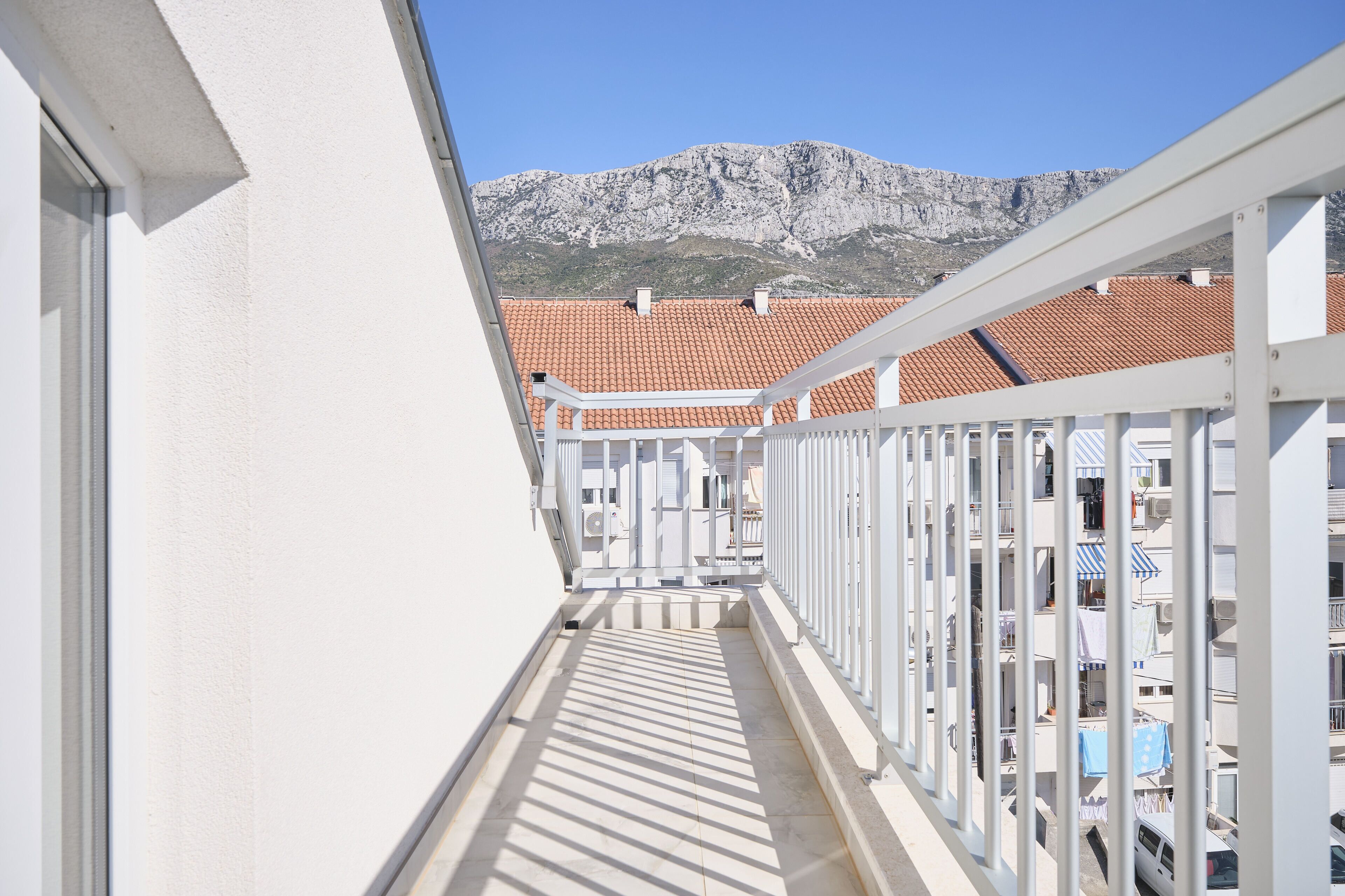 A balcony with a mountain view, white railings, and red-tiled roofs in the background.