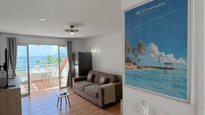Ein modernes Wohnzimmer mit großem Fenster, einer Couch, einem Fernseher und einem Essbereich mit Meerblick.