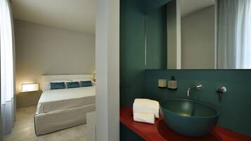 Habitación de hotel con una cama, una mesita de noche con lámpara, una encimera roja con lavabo y espejo, y un tazón azul.