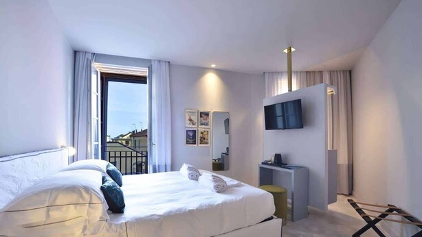A modern hotel bedroom with a large bed, a TV, and a balcony. - Boutique Hotel De La Ville Laigueglia (Laigueglia)
