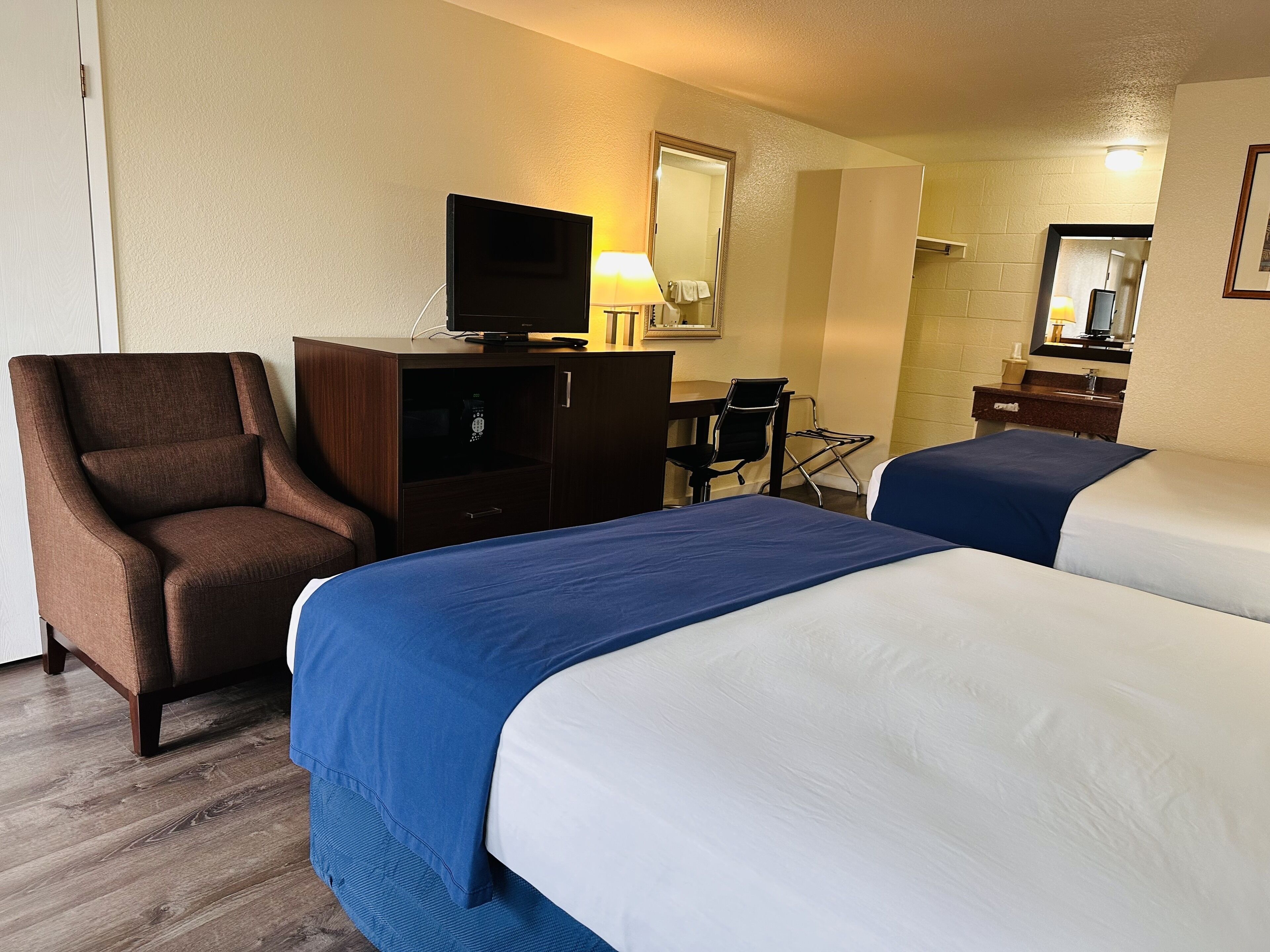 Una habitación de hotel con dos camas, un escritorio, una silla, un televisor y un espejo.