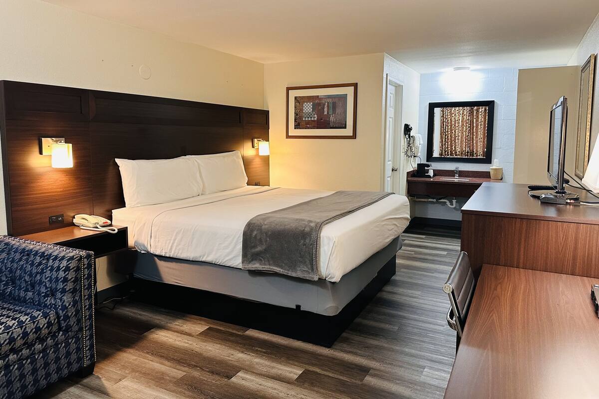 Una habitación de hotel con una cama grande, lámparas de noche, un escritorio, una silla y un espejo.