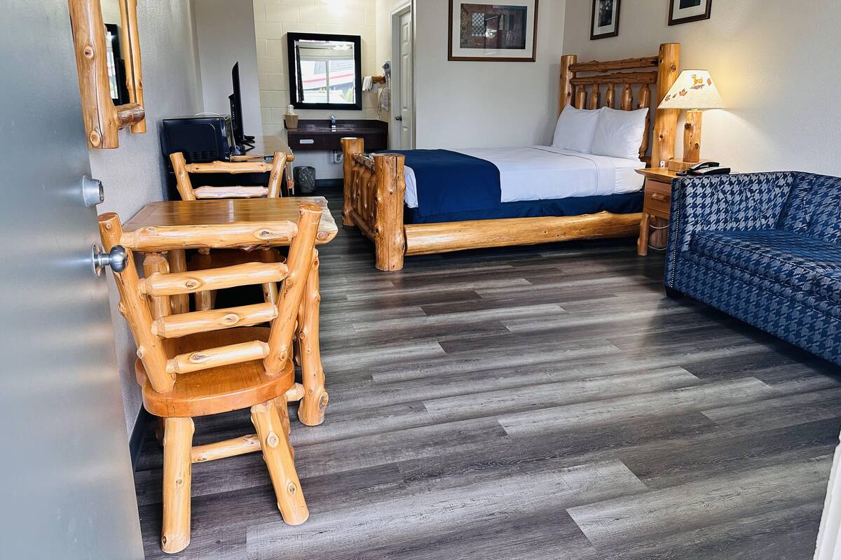 Una habitación con una cama de madera, un sofá, una mesa de comedor con sillas y un televisor.