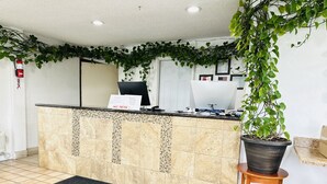Een receptiegedeelte met betegelde vloer, een receptiebalie, een computer en een potplant.