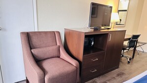 Een hotelkamer met een losse, roze fauteuil, een houten bureau met een televisie en een bureaulamp.