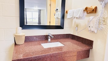 A bathroom with a granite countertop sink, a mirror, a hairdryer, and a towel rack.