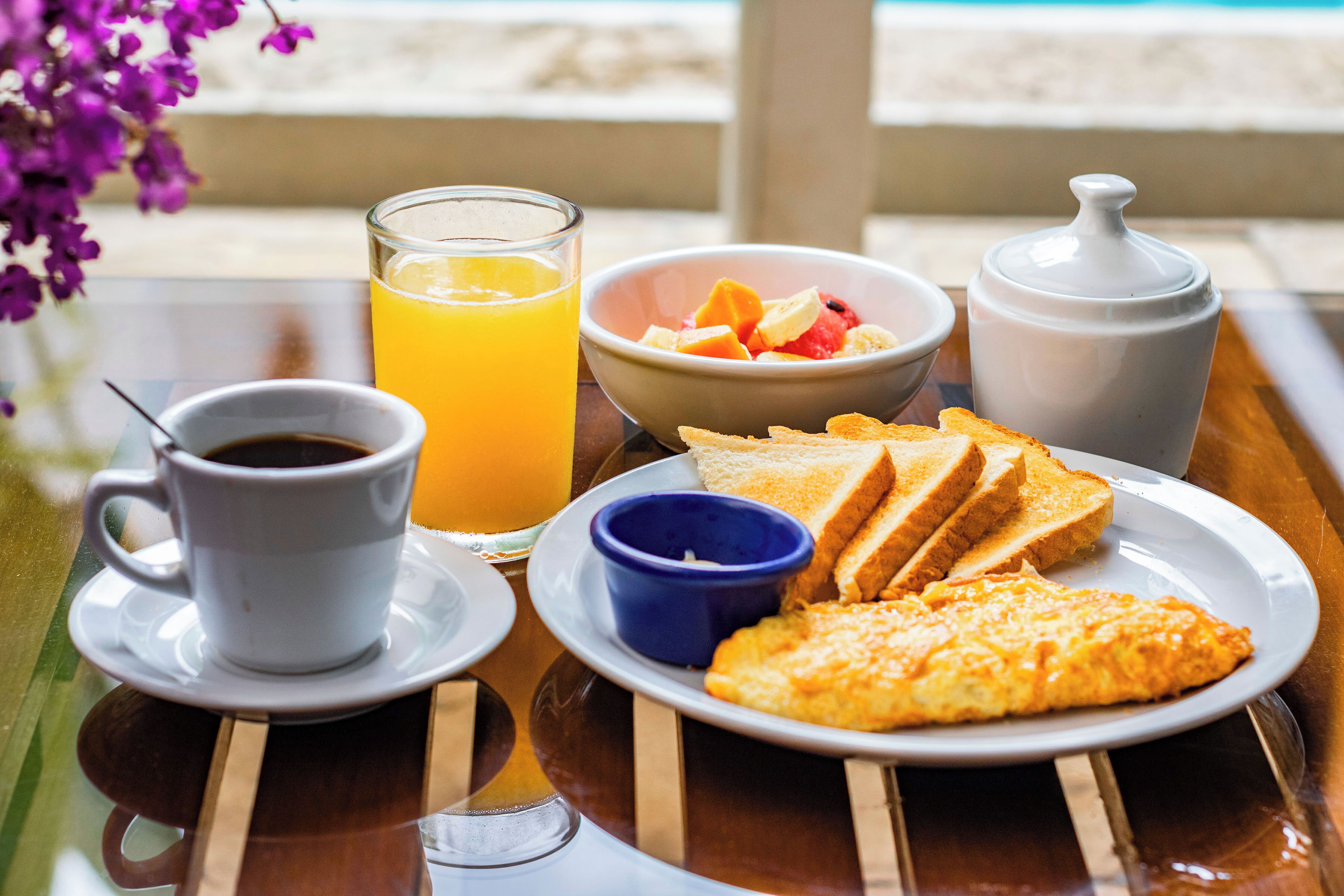 Bandeja de café da manhã com torradas, ovos mexidos, uma tigela de fruta, um copo de suco de laranja e uma xícara de café.