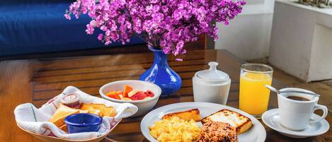 Une table mise pour le petit-déjeuner, avec un vase de fleurs, un bol de fruits, des toasts, des œufs brouillés et un verre de jus d’orange.