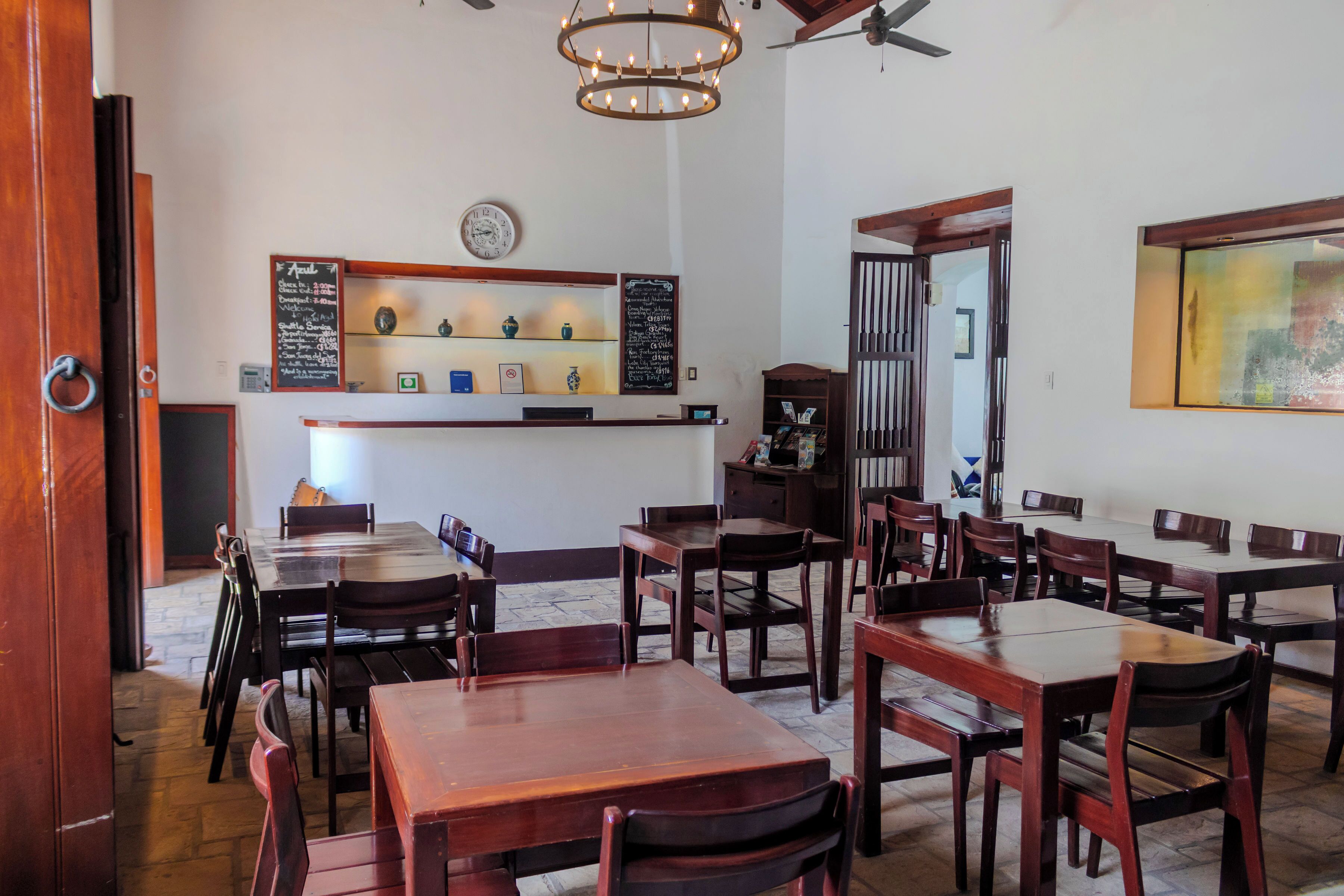 Interior de restaurante con mesas y sillas de madera, un menú en la pizarra y un reloj en la pared.