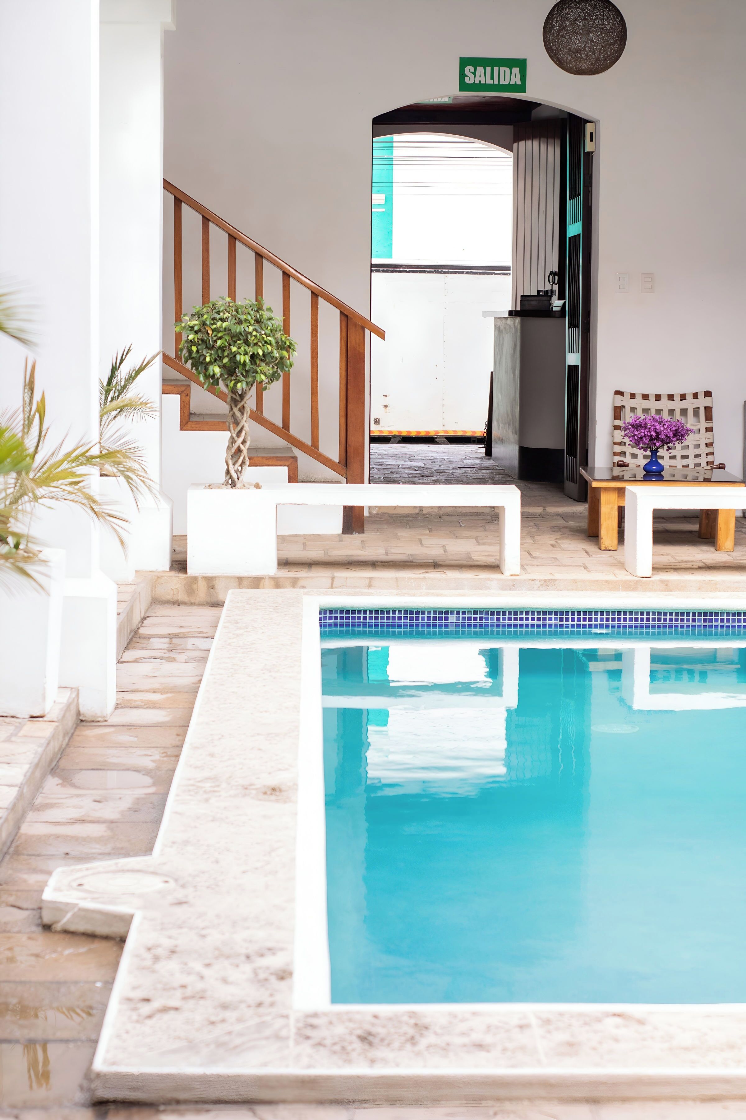 A pool area with a sign reading 'SALIDA,' a staircase, and a small table with a vase of flowers.