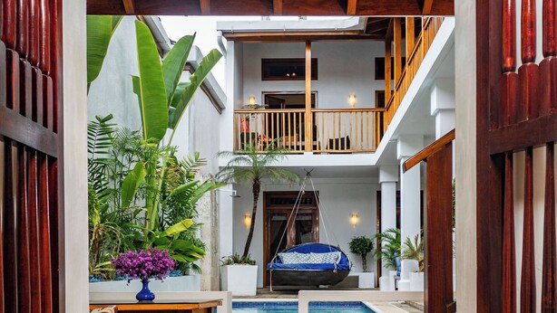 Un área de piscina interior con techo de madera, una mesa con un florero y vistas a un balcón en un segundo piso.