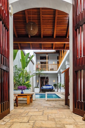 An indoor pool area with a wooden ceiling, a table with a vase of flowers, and a view of a second-floor balcony. - Hotel Cafe Azul  (León)
