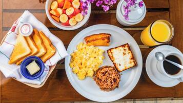 A breakfast table with toast, scrambled eggs, fried rice, and a fruit bowl.