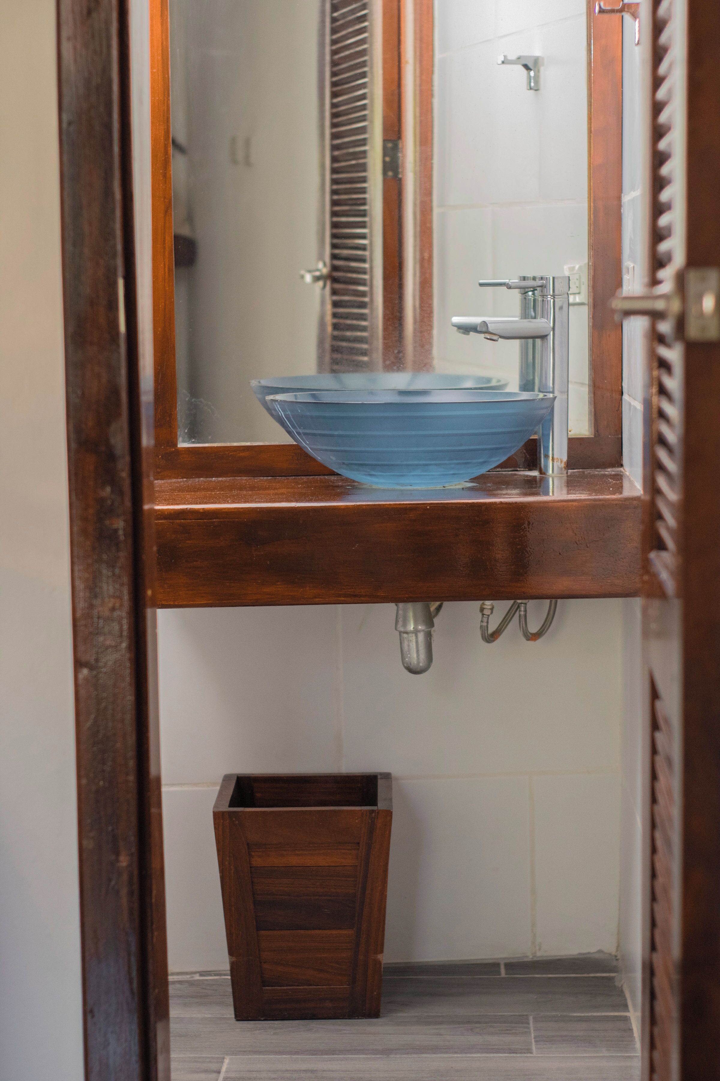 A bathroom with a wooden vanity, a blue vessel sink, a mirror, and a wooden waste basket.