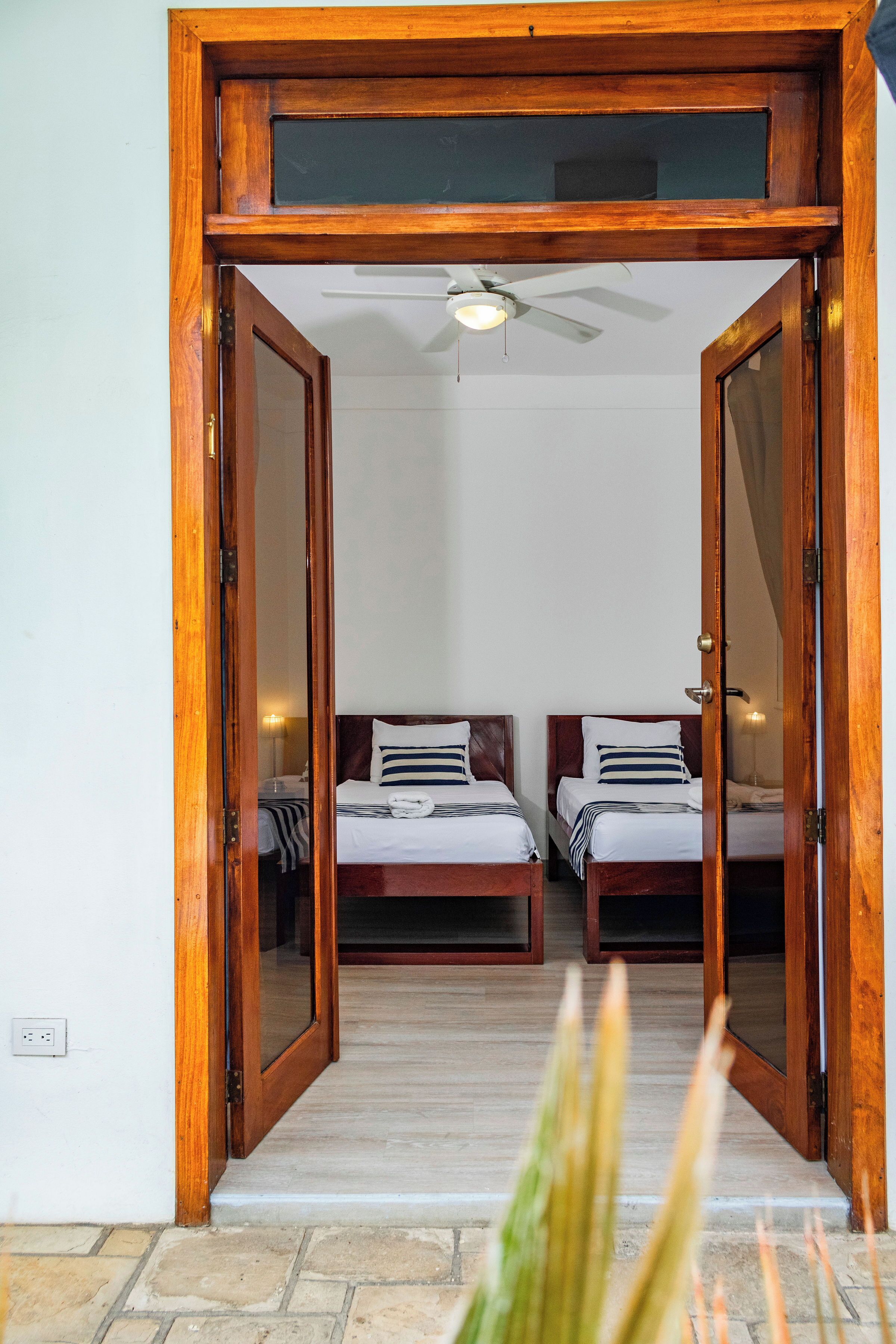 Ein Zimmer mit zwei Betten, einem Deckenventilator und einer Holztür.