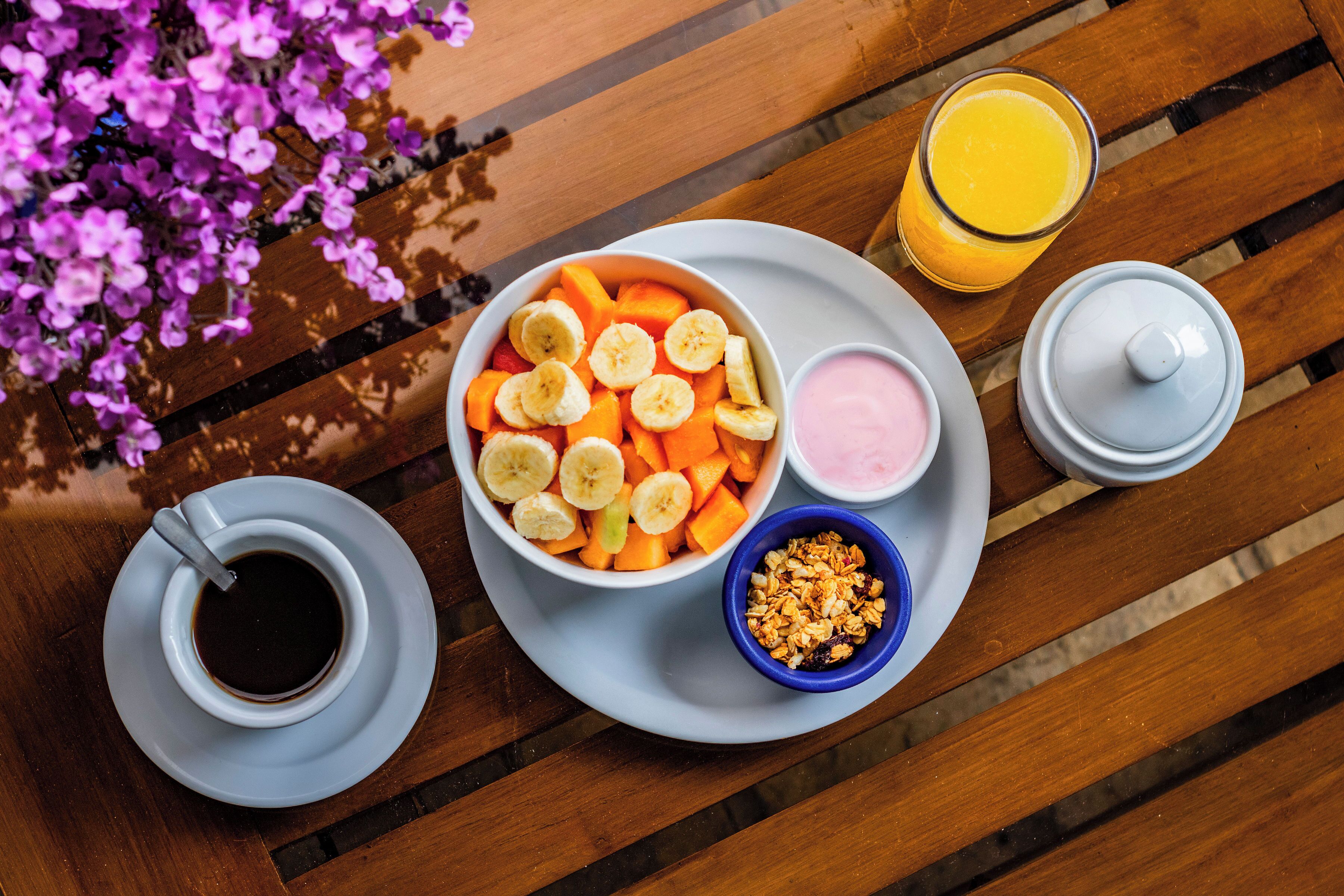 A breakfast setup with a bowl of fruit, a glass of orange juice, a cup of coffee, and a small bowl of granola on a wooden table.