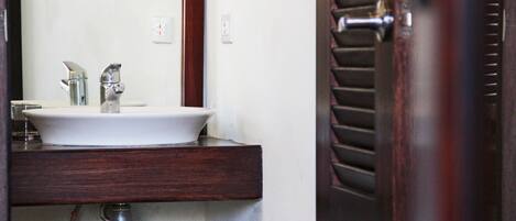 Un baño con lavamanos blanco, espejo y tocador de madera.