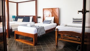 Una habitación con dos camas, cabecero de madera, mesita de noche, lámpara y suelo de baldosas.