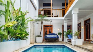 Un área de piscina con una hamaca colgante, plantas y un balcón.