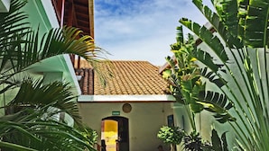 Un patio con techo de tejas, una puerta que dice "SALIDA" y abundante vegetación verde.