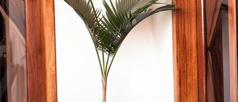 A potted plant in a corner with wooden doors and a tiled floor.