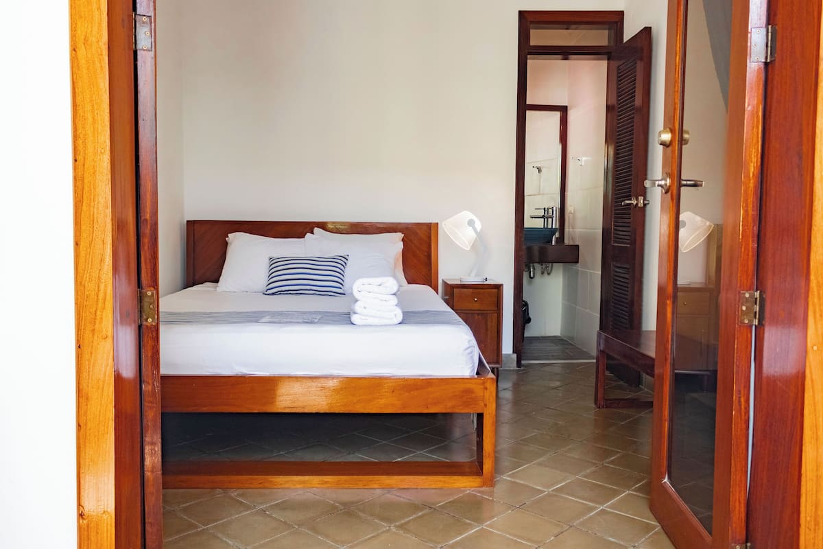 Uma cama de madeira com roupa de cama branca, uma luminária de cabeceira e um travesseiro listrado.