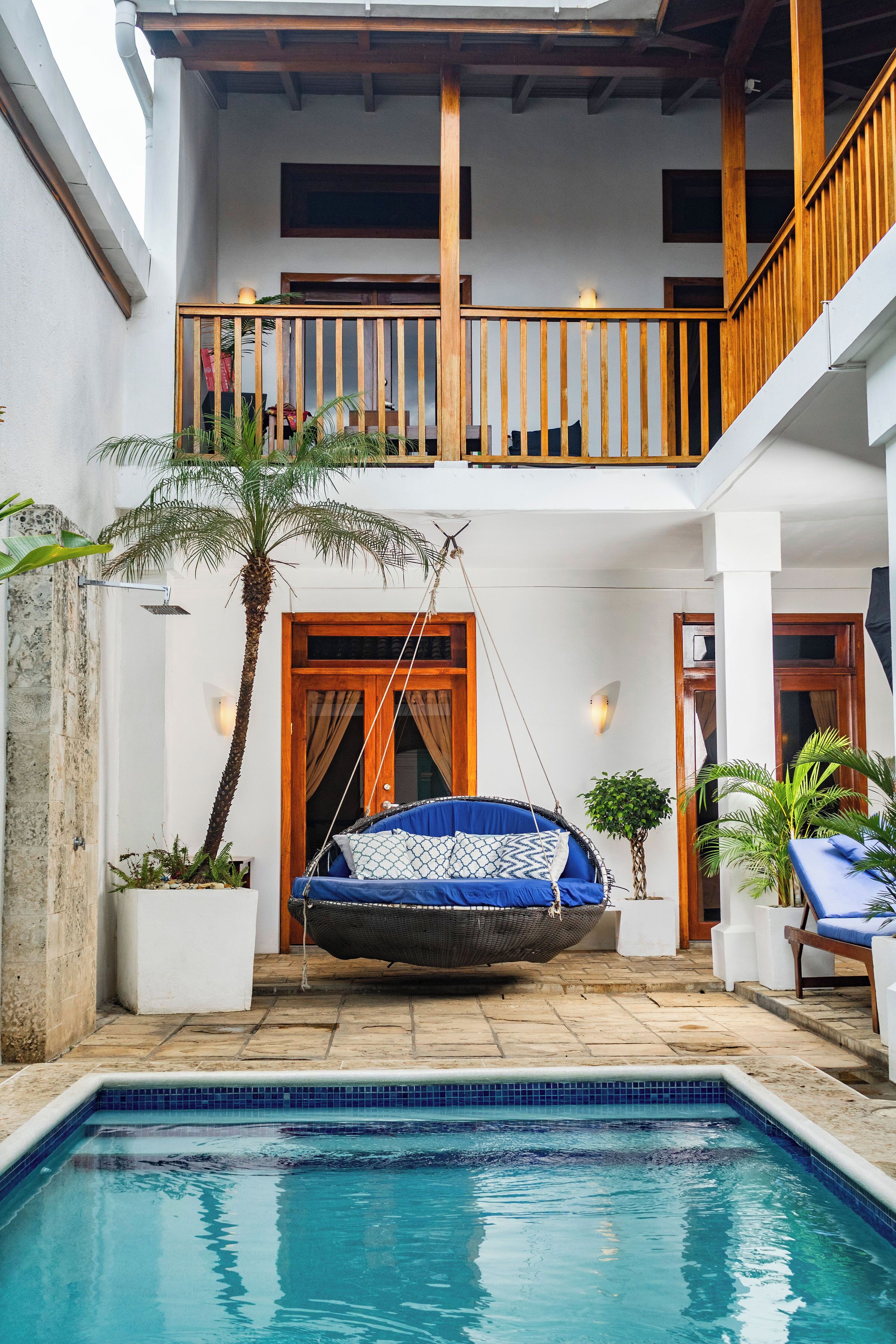 A pool area with a hanging chair, a palm tree, and a wooden balcony.