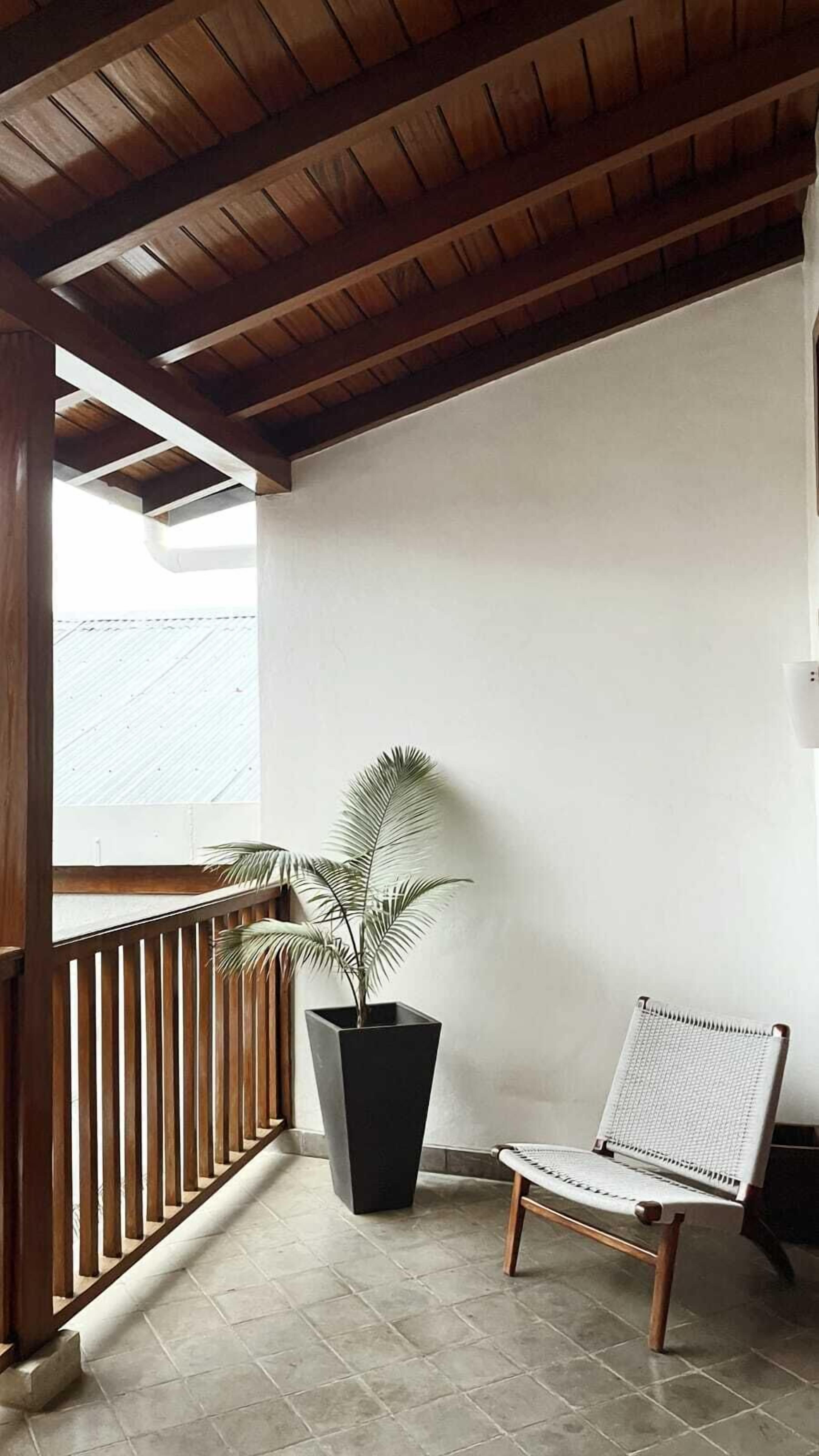 Un balcón con barandilla de madera, una planta en maceta y una silla de mimbre.