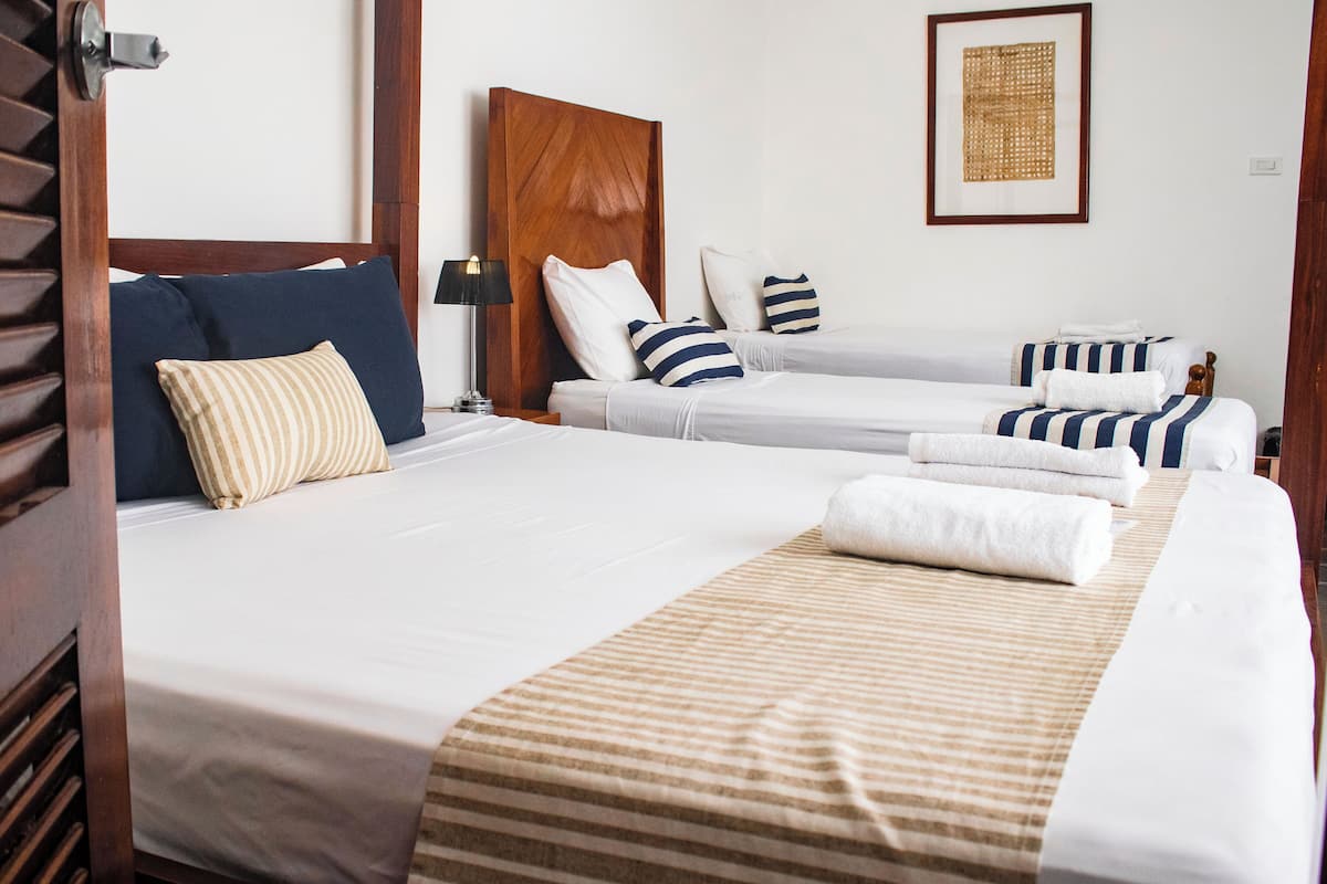 Quarto de hotel com duas camas, cabeceira de madeira, roupa de cama listrada, uma obra de arte emoldurada na parede e uma mesa de cabeceira com abajur.