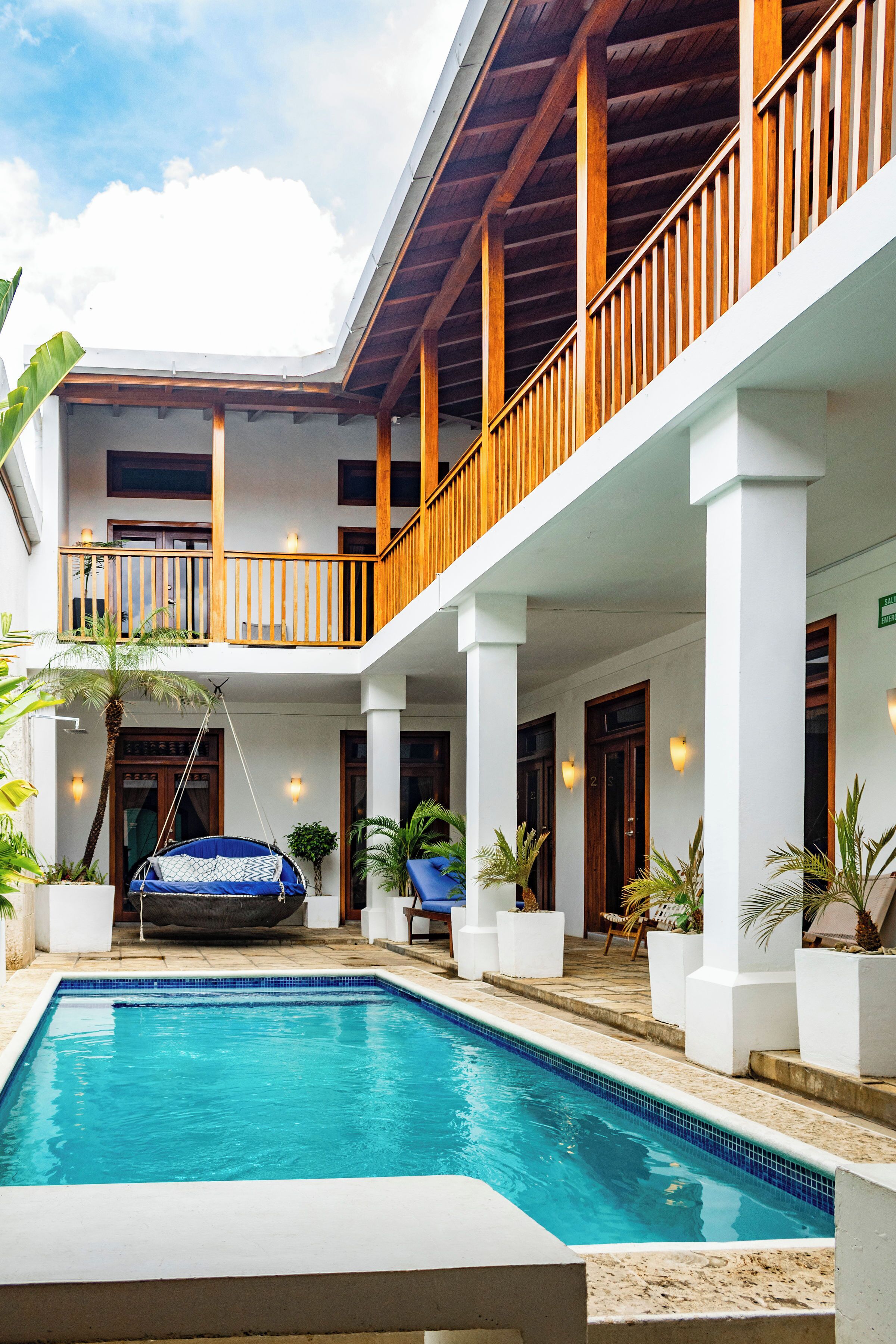 A pool area with a hanging chair, a wooden balcony, and a two-story building with columns.