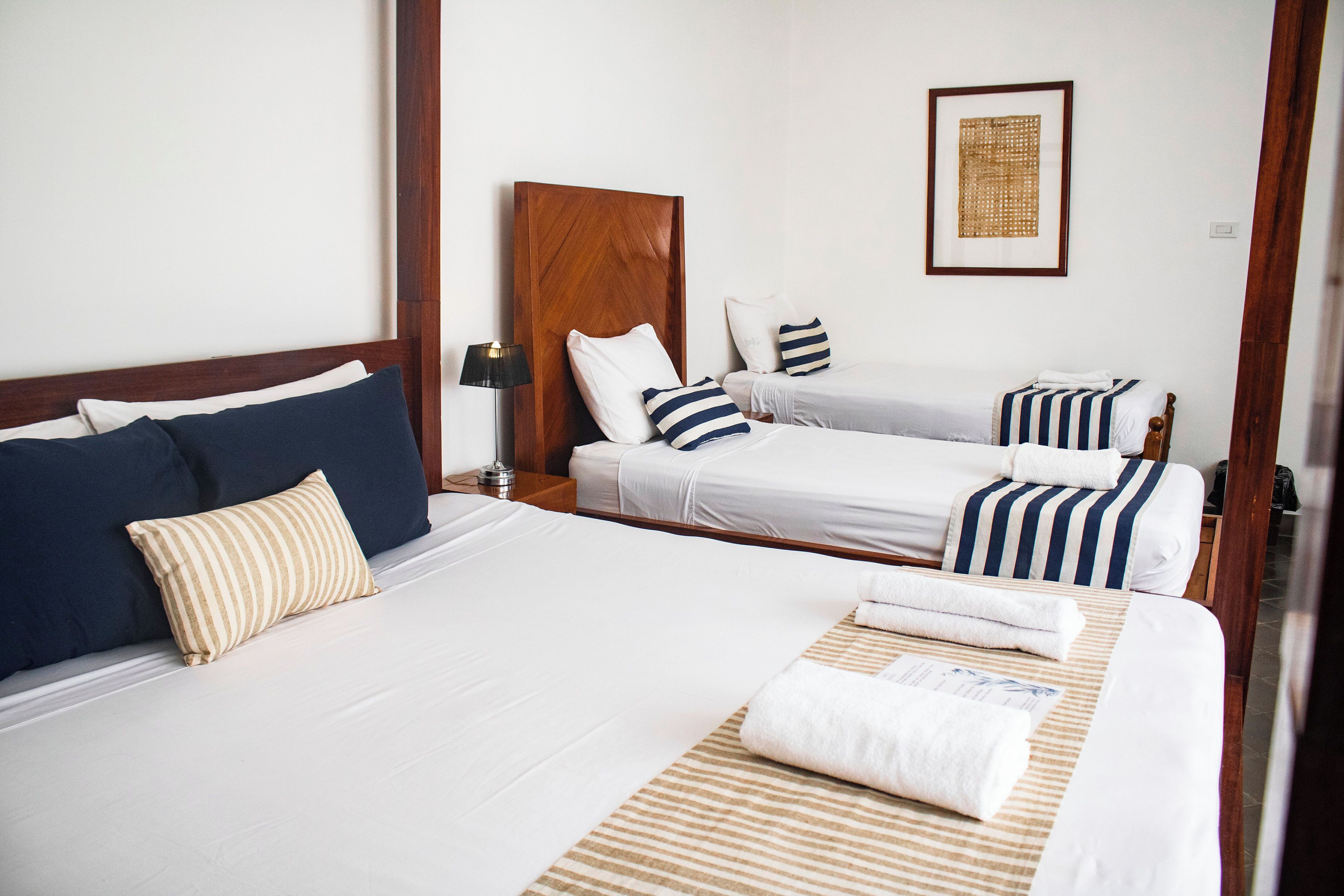 Ein Hotelzimmer mit zwei Betten, einem Holzkopfende, weißer Bettwäsche, gestreifteren Kissen, einer Lampe und einem gerahmten Kunstwerk an der Wand.