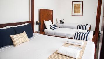 Habitación de hotel con dos camas, cabecero de madera, ropa de cama blanca, almohadas a rayas, una lámpara y una obra enmarcada en la pared.
